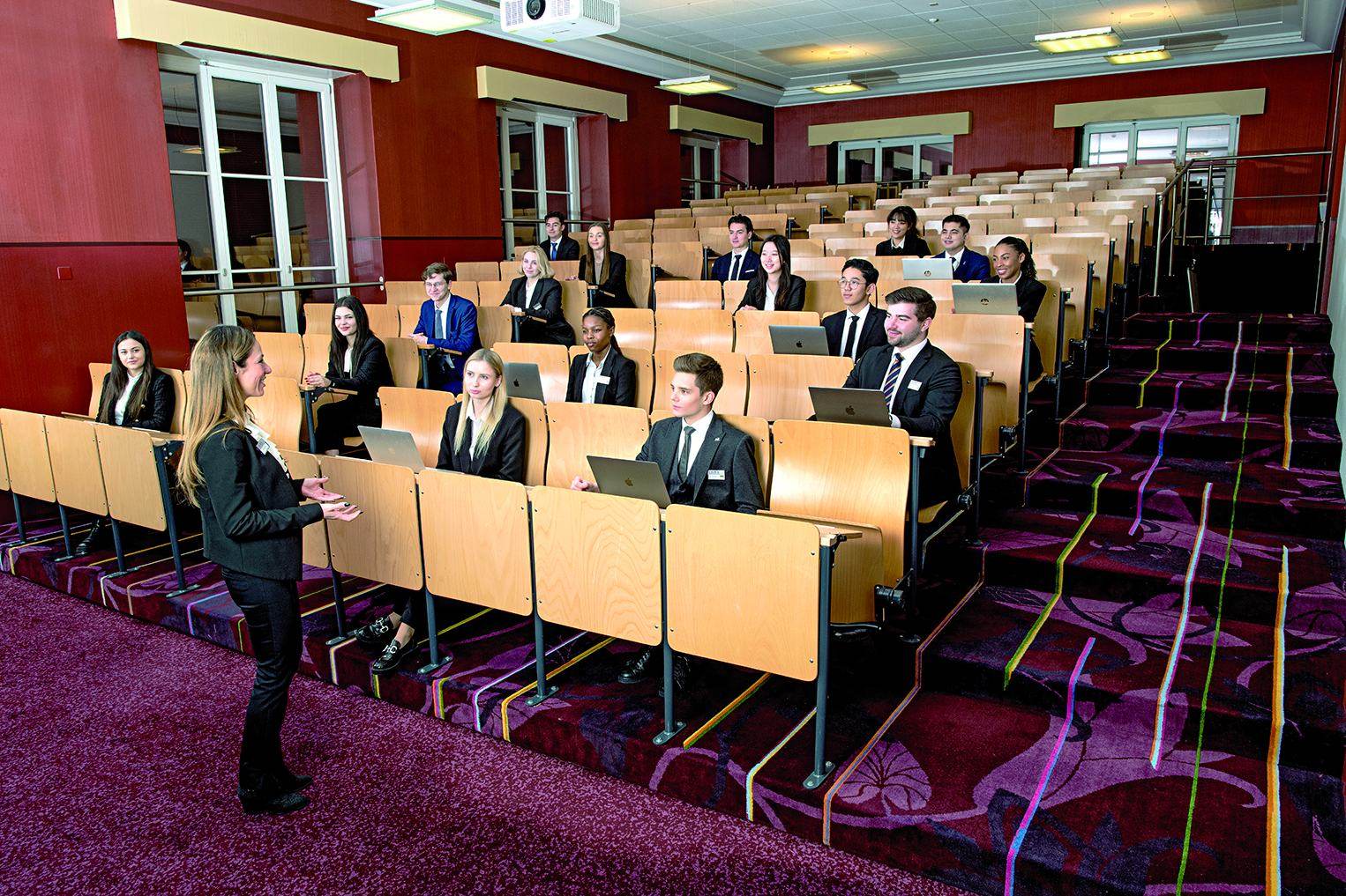 Students in business dress with laptops in the tiered BHMS lecture theater